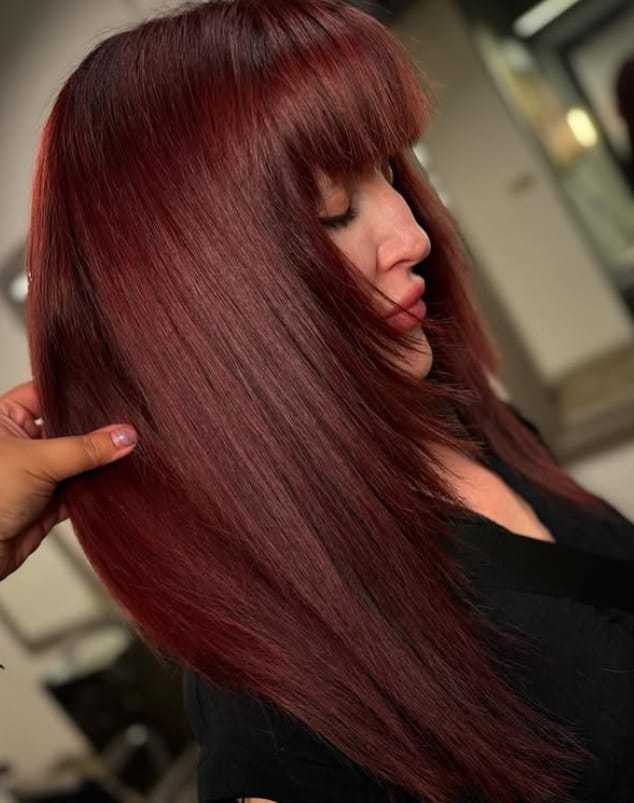 Red-haired woman with straight locks and bangs, styled in a salon setting.