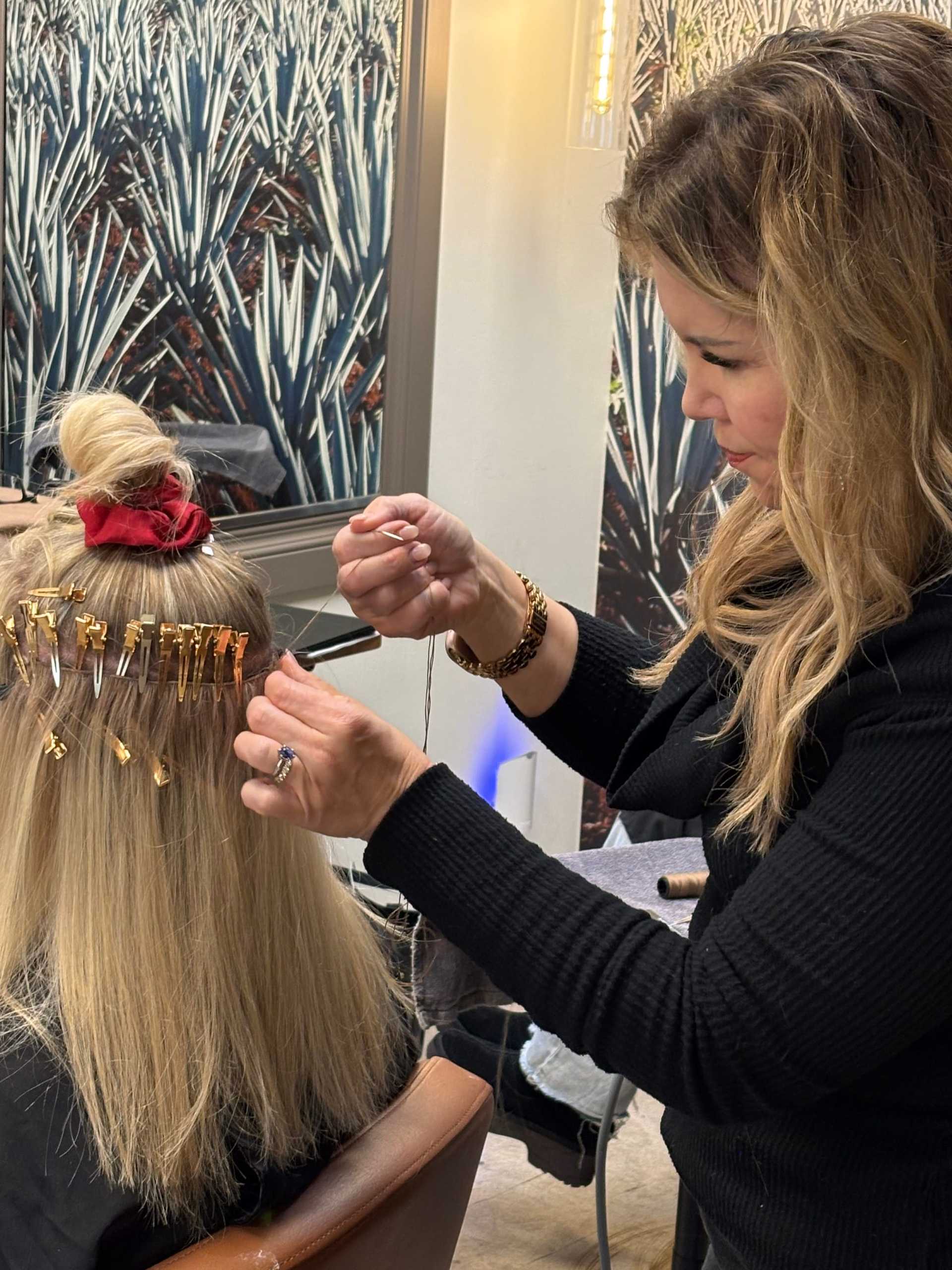 Hairstylist attaching hair extensions to a woman's blonde hair in a salon.