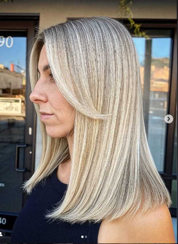 Woman with sleek, straight, blonde hair in a salon setting, showcasing a layered hairstyle.