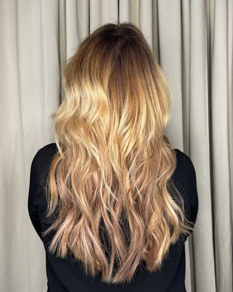 Long, wavy blonde hair with subtle highlights, styled against a curtain backdrop.