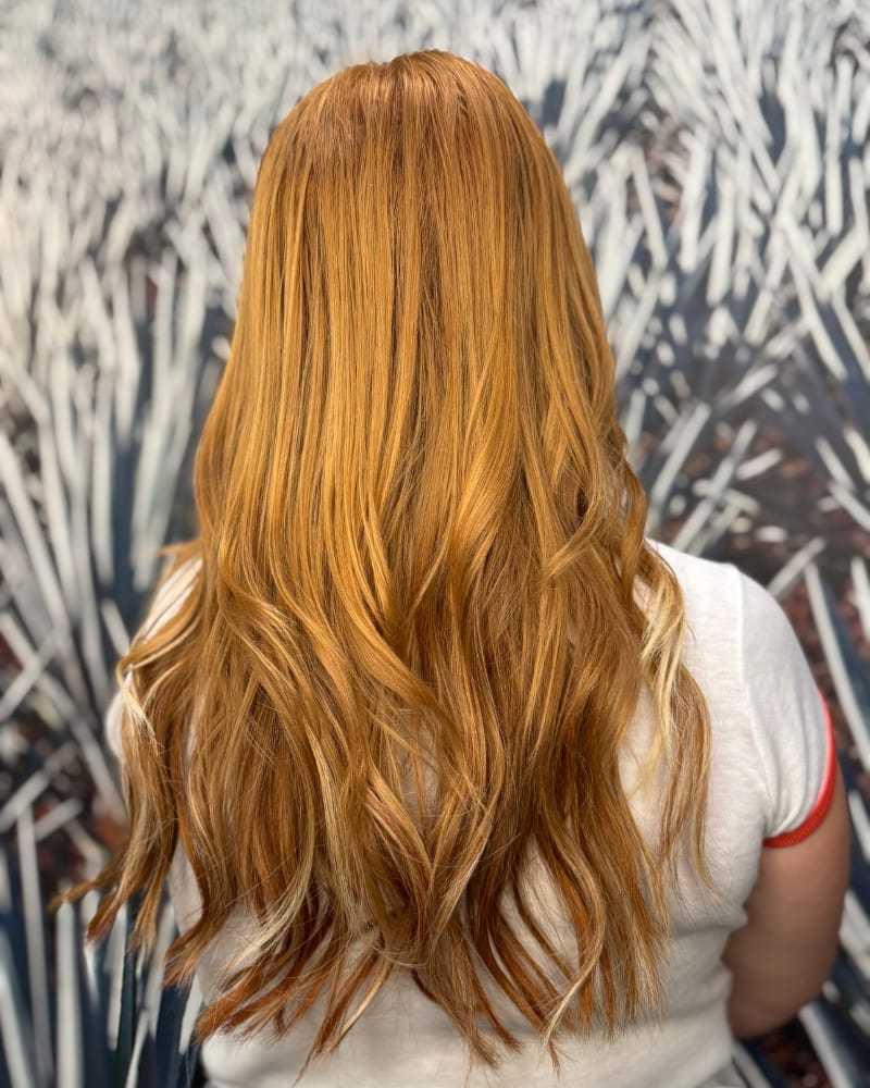 Red-haired woman with wavy hair, facing a field of blurred white plants.