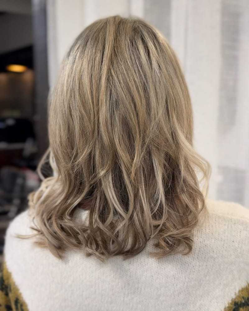 Back view of wavy, shoulder-length, blonde hair in a cozy indoor setting.