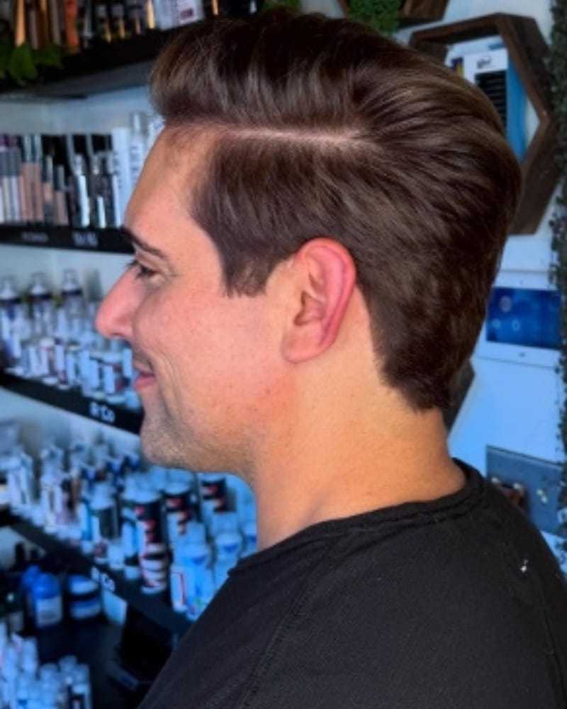 Man with styled hair in a salon, shelves of hair products in the background.